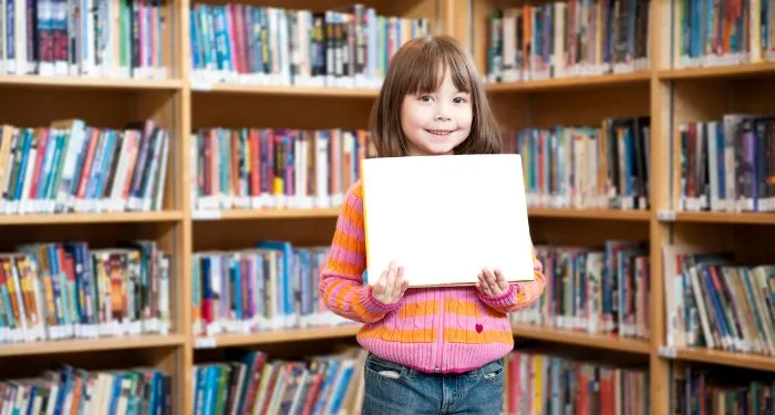 child in a library holding up a picture book standing in front of bookshelves