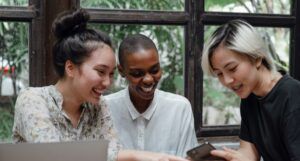 three friends at a cafe laughing and looking at a cell phone