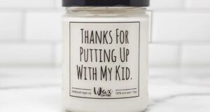 a white candle in a glass jar with a black lid and black text that reads 'Thanks for Putting Up with My Kid"