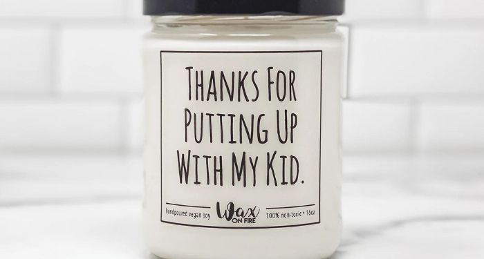 a white candle in a glass jar with a black lid and black text that reads 'Thanks for Putting Up with My Kid"