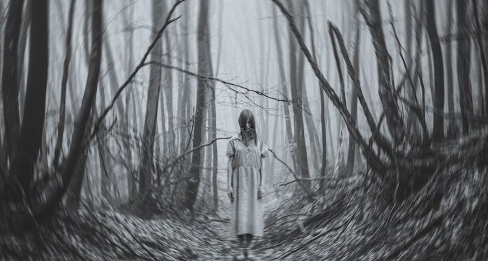 an unsettling black and white photo of a girl in a white nightgown in the woods