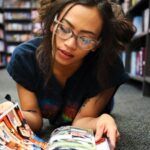 tan-skinned girl reading comics on the floor