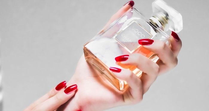 very fair-skinned hands with red polish holing a perfume bottle