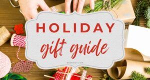 red text in a white banner that reads "Holiday Gift Guide." in the background, hands wrapping small boxes in brown paper with white string and green accents