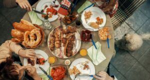 Image of several people around a table full of food. There is a dog on the floor looking up.