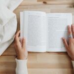 a photo of someone's hands as they are reading a book that is on a table