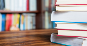 a photo of a stack of books on a table with a bookshelf in the background