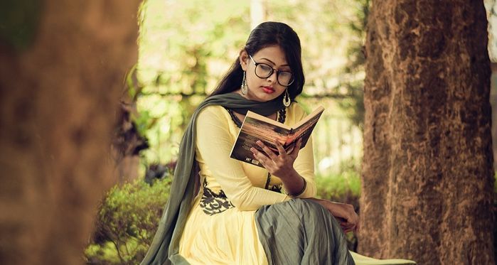 tan-skinned Indian woman dressed in a sari reading a book on a bench