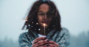 brown-skinned teen with a sparkler outside while it's snowing