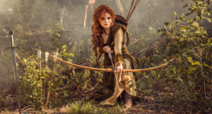 a photo of a woman crouching while shooting a bow in a forest. She's wearing medieval clothing