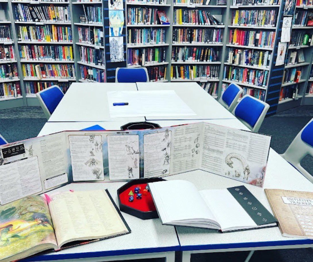 a table containing various D&D items, a DM screen, dice and books.