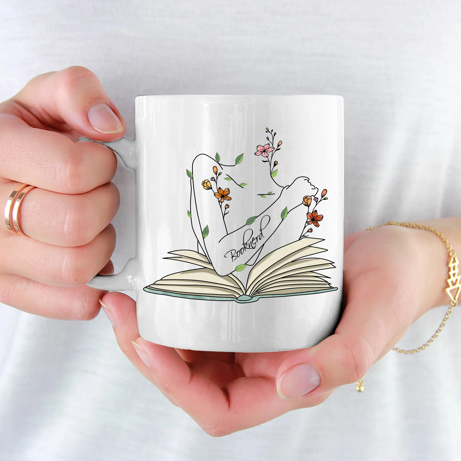 white mug depicting the line art of a woman above an open book, with orange and pink florals