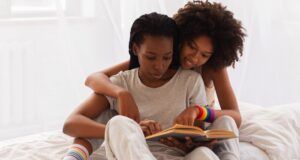 brown-skinned Black women cuddled up and reading in bed together