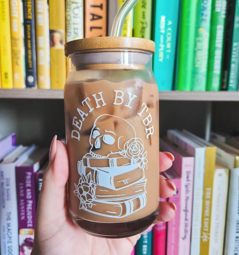 Image of a glass with a lid held by a white hand in front of bookshelves. In white on the glass are the words 