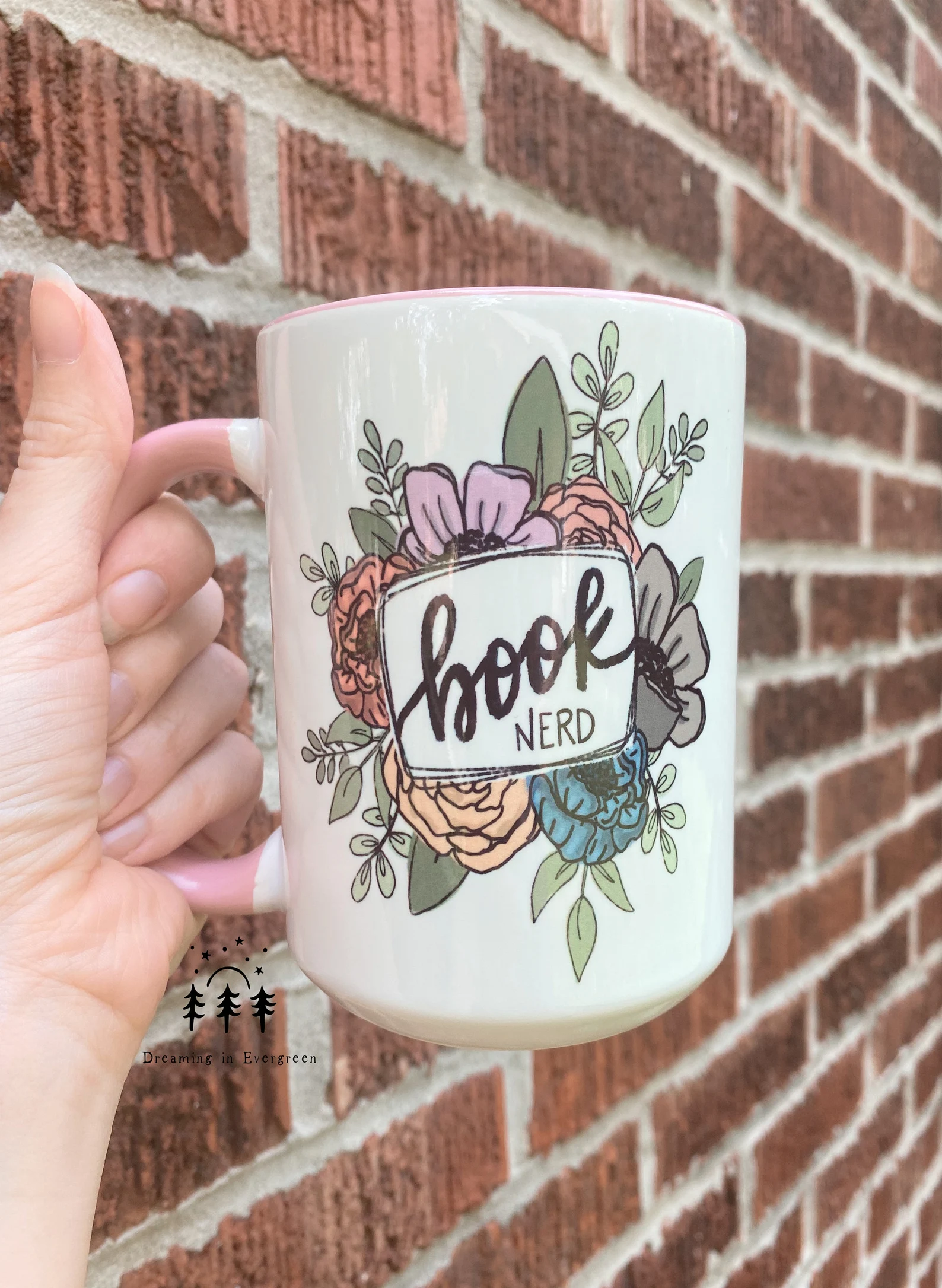 a white and pink mug with orange, pink, blue, and brown blossoms that reads "book nerd"