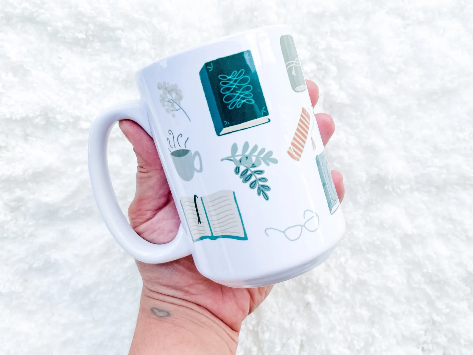 white mug with a vintage flatlay style of illustration that depicts books, glasses, mugs, and plants