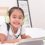 Image of an Asian girl wearing headphones on a bed with a tablet