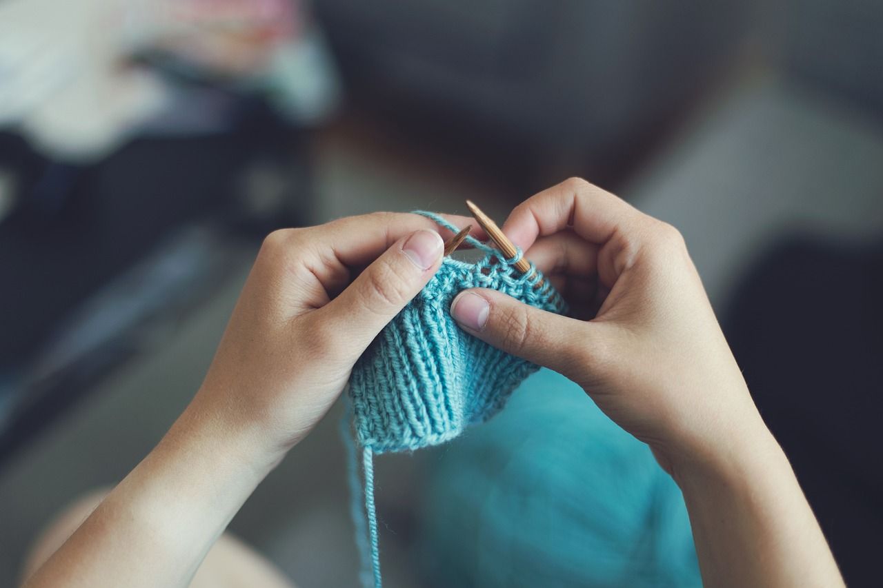 A pair of hands knitting a small, light blue square.