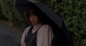 Moody image of a Black woman in victorian clothing holding a black umbrella