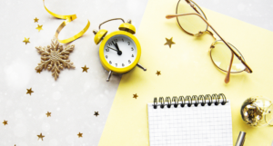 a photo of a notepad, glasses, and a yellow alarm clock on a yellow background with gold star confetti