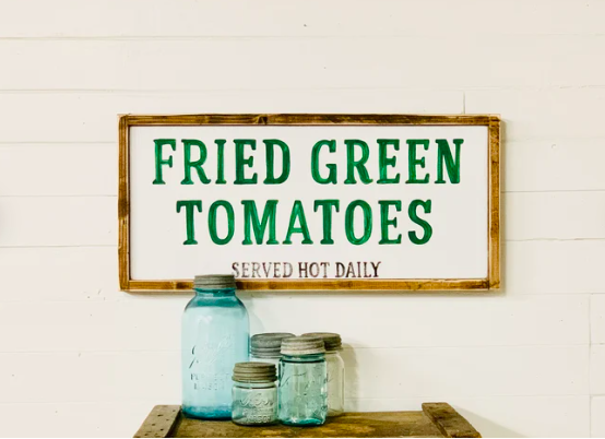 Framed wall art of a cafe sign that says "Fried Green Tomatoes, served hot daily" in green font
