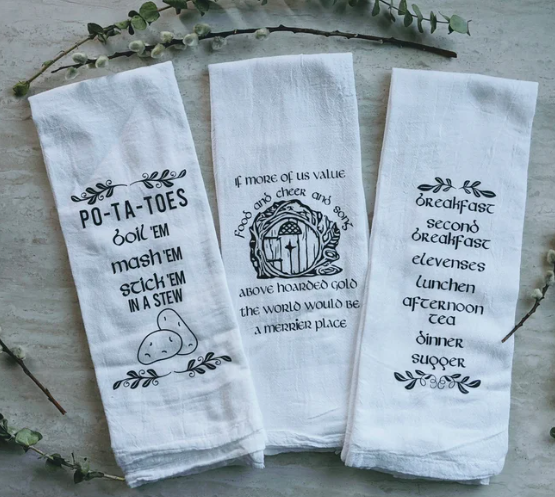 Three white tea towels with various Lord of the Rings quotes about food screen printed on. 