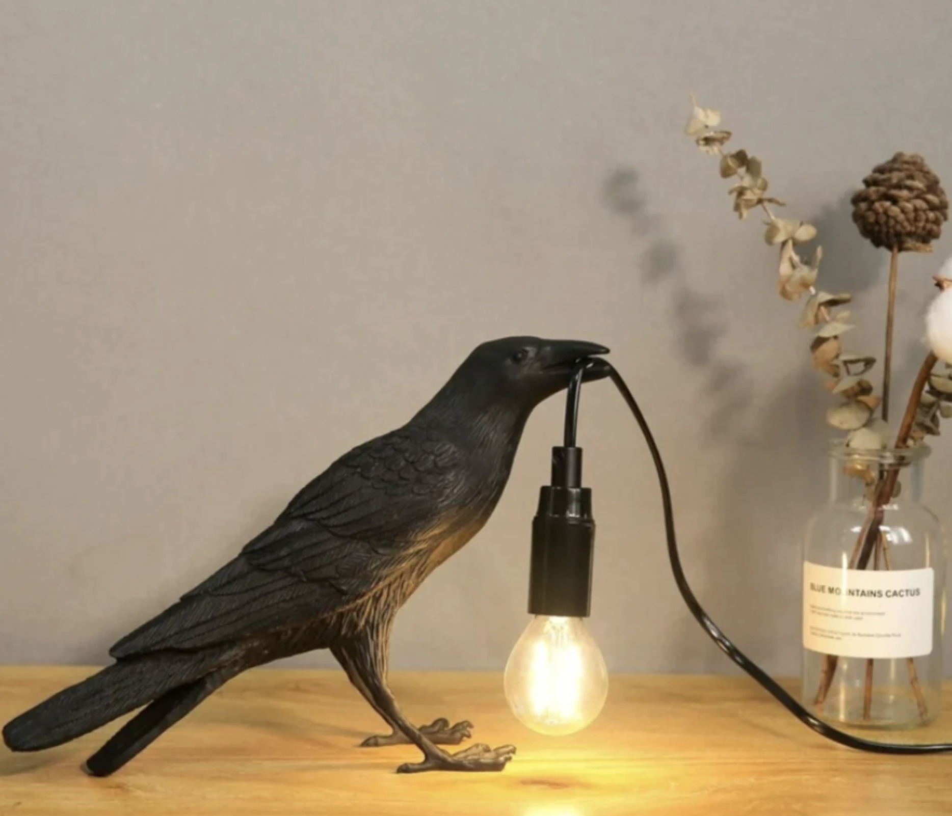 A black crow statue holding a lightbulb in its beak as a lamp.