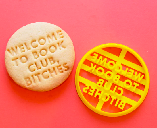 Plastic cookie cutter and cookie baked with it that says "Welcome to book club, bitches"