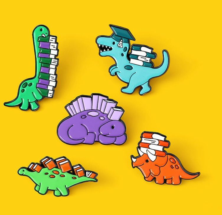 Image of five different dinosaurs carrying books or wearing them as armor. The pins are on a yellow background. 