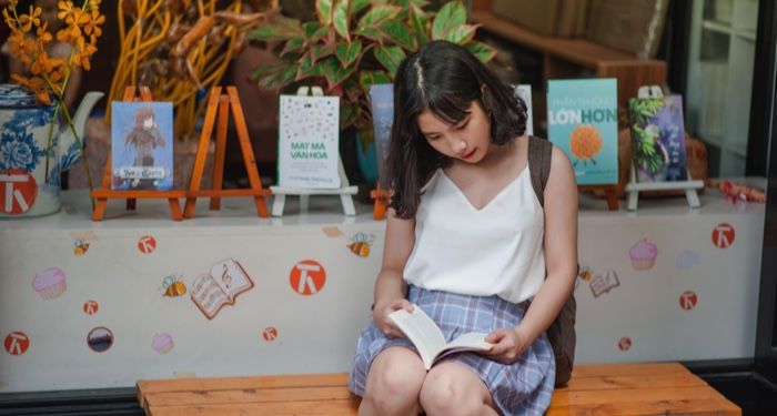 fair skinned Asian woman reading on a library bench