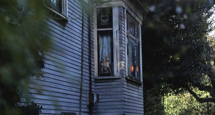 exterior of a wooden house with a lamp without a shade and a rabbit doll seen in a bay window