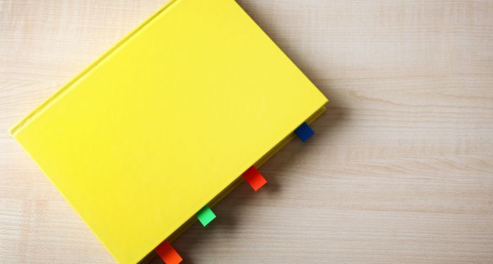 Image of a yellow book on a wood background. The book has sticky tabs on the pages
