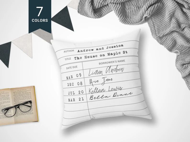 Photo of a white pillow with a neat personalised print of a library card, some glasses on a book on the left side and a spread grey blanket on the left. 