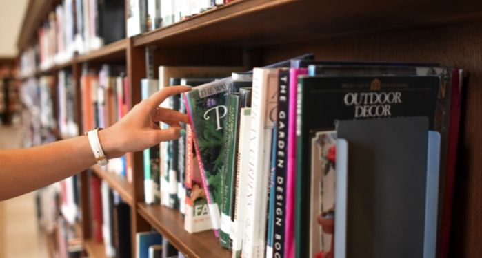 a hand pulling a book from a library shelf