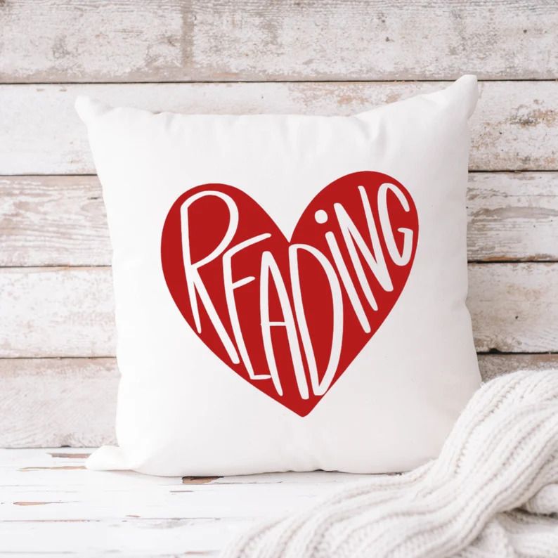 Photo of a white pillow with a red heart at the centre with white letters saying reading in the shape of the heart.