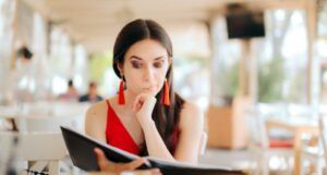 woman in a red tank top and dangly red earrings smirking while reading a book