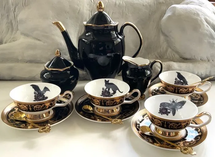 a photo of a black gold porcelain tea set with illustrations of cats, bats, moths, and a crow in the cups