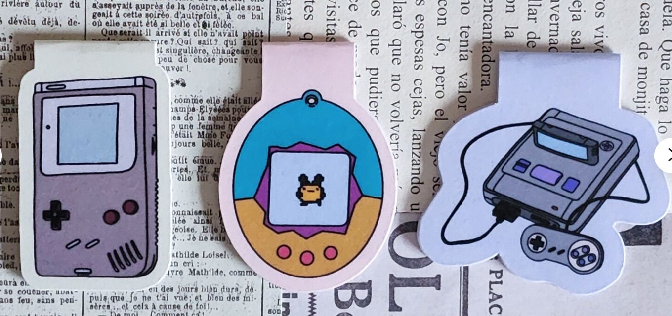 Image of three small magnetic bookmarks. Left to right: image of a gameboy, image of a tomagotchi, and image of a sega.