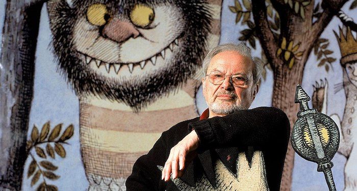 a photo of Maurice Sendak with images from Where the Wild Things Are behind him