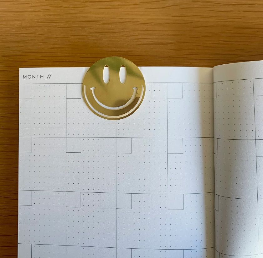 Image of a metal bookmark in the shape of a smiley face. 