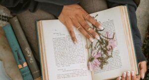 brown, manicured hands holding a book open with dried flowers inside it