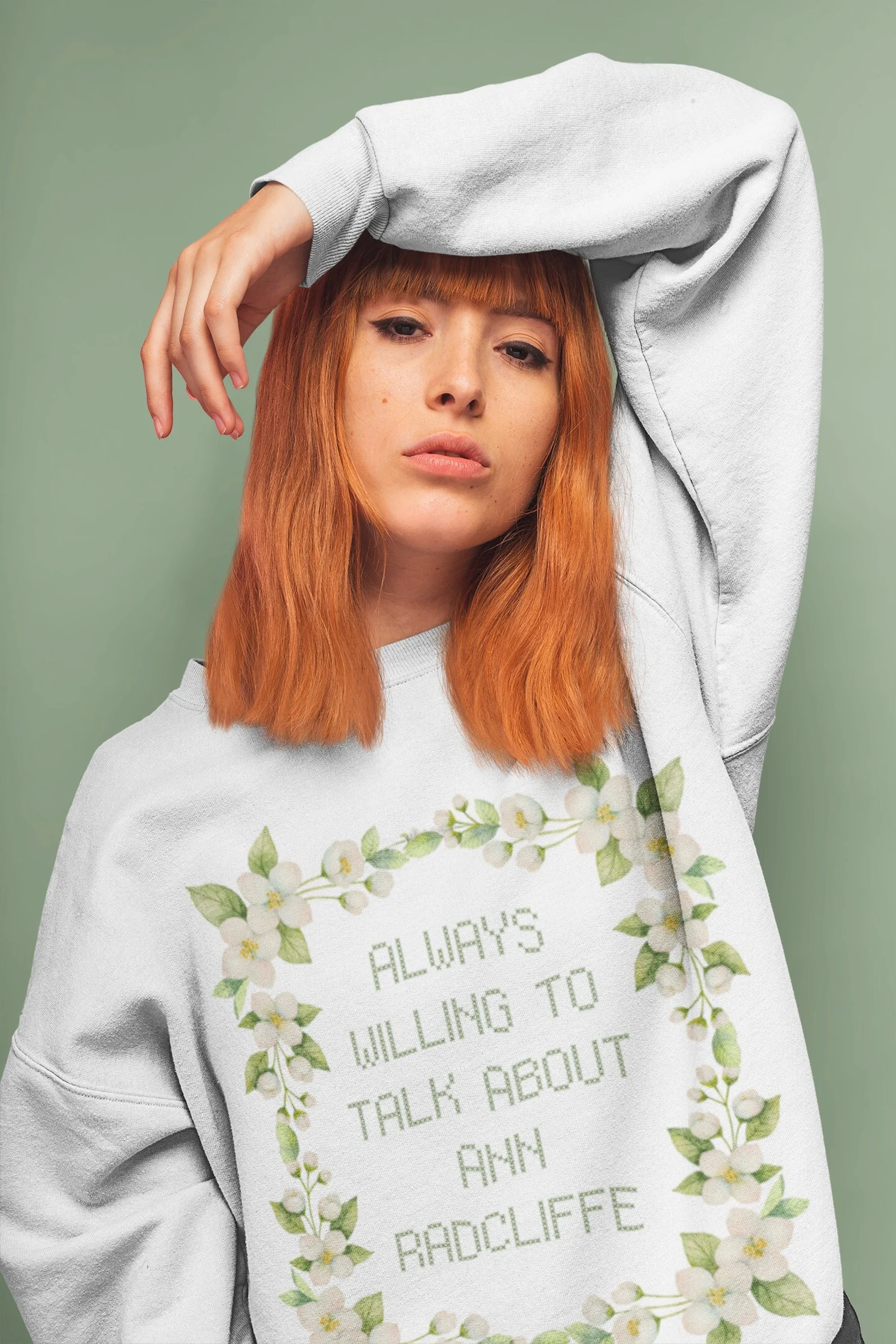 A person wearing a sweatshirt with cross-stitch-looking text reading "Always Willing to Talk About Ann Radcliffe" and a floral border