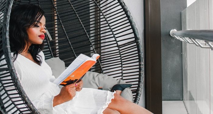 brown-skinned Black woman with red lipstick reading in a wicker chair