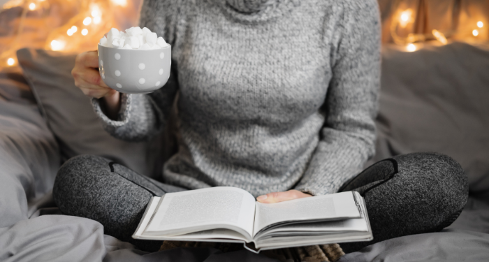 a photo of a woman in a cozy sweater with a mug with marshmallows, reading