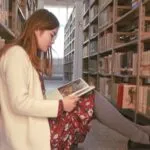 fair-skinned Asian woman sitting on the floor of a library reading