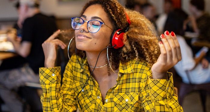 a photo of a Black woman in a cafe listening to headphones with her eyes closed, smiling