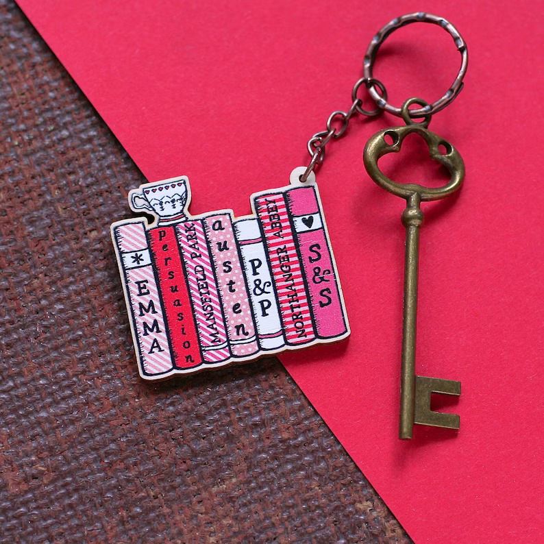 Photo of keychain with books side by side and the spines showing titles of Jane Austen's book, with a teacup on top.