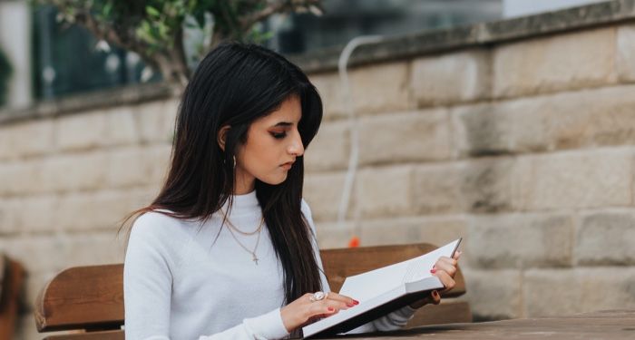 olive-skinned woman with long dark hair reading at a wooden table