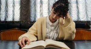 lighter-skinned woman with dark, curly hair and a cardigan on reading