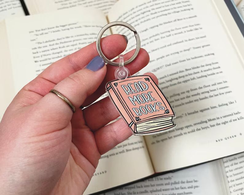 Photo of a keychain shaped like a book in the colour pink and the text Read more books on the cover